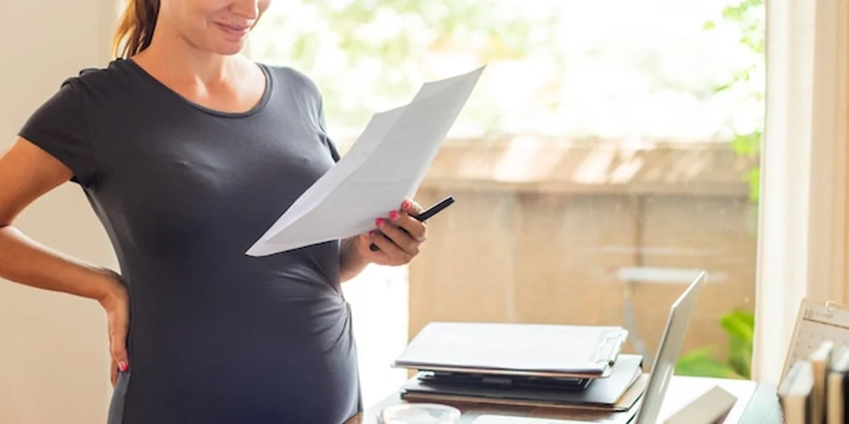 Kobieta w ciąży czyta dokumenty przy biurku