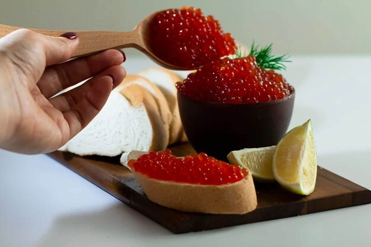 Czerwony kawior w naczyniu ceramicznym na drewnianej platformie na białym tle