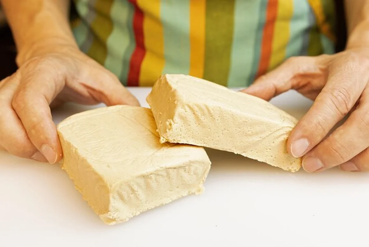 Osoba w zielonym fartuchu kroi blok tofu w kuchni