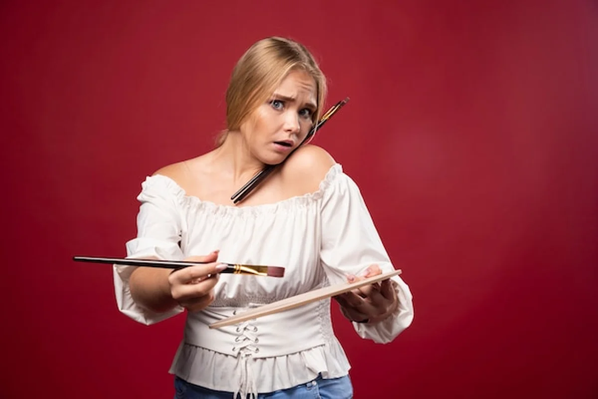Blondynka trzyma paletę i pędzle, wyglądając na zaskoczoną i zdezorientowaną