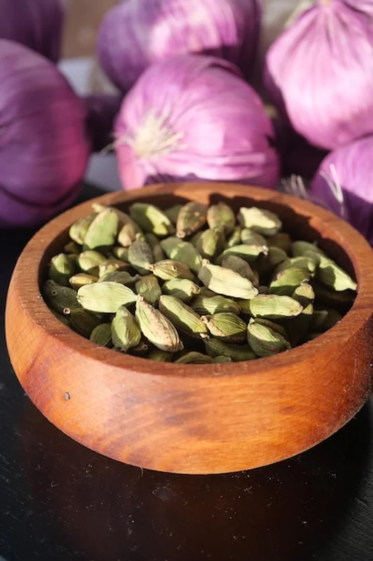 Nasiona kardamonu w drewnianej misce z fioletową cebulą