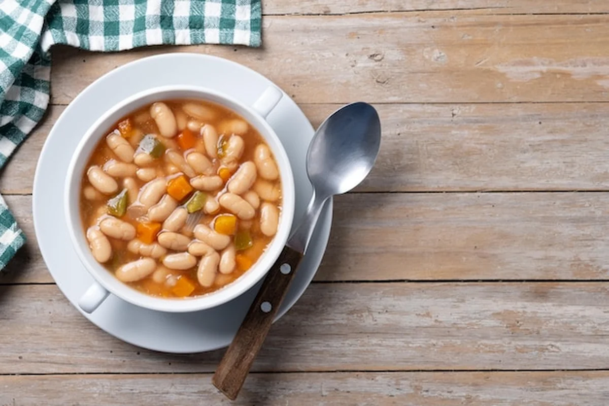 Zupa fasolowa z warzywami w białej misce na drewnianym stole