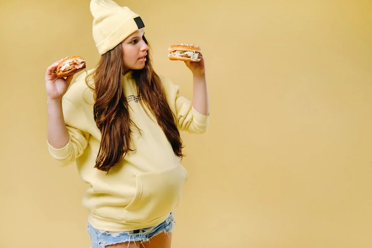 Ciężarna dziewczyna trzymająca hamburgery na żółtym tle