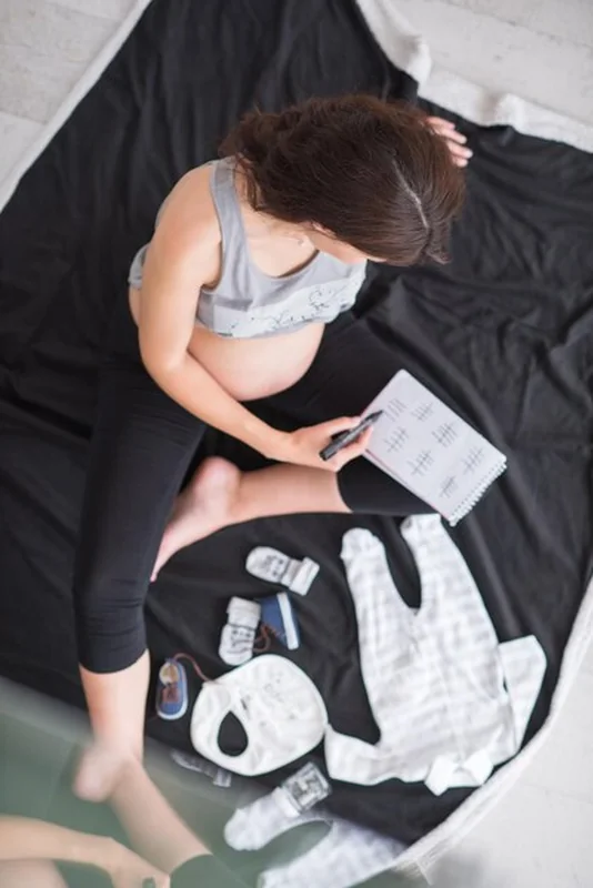 Kobieta w ciąży na podłodze sprawdzająca listę ubrań dla niemowląt